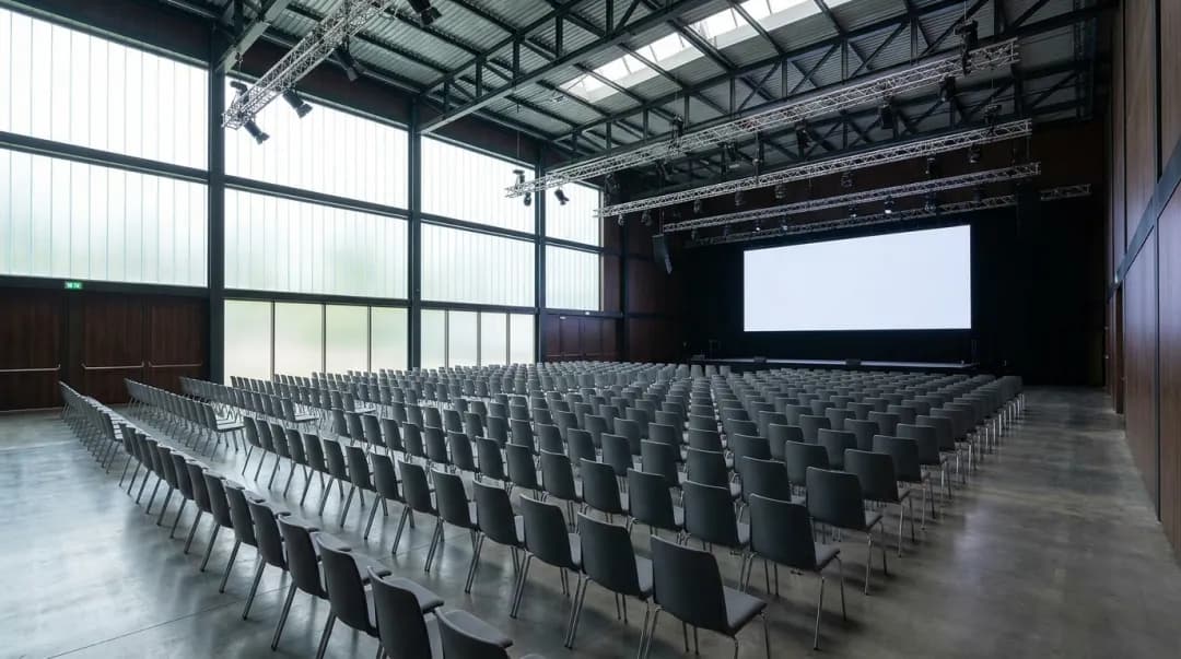 Salão de convenções corporativo montado com cadeiras e telão, pronto para receber o público