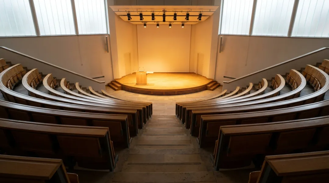 Auditório universitário moderno e iluminado com fileiras de poltronas voltadas para um palco, pronto para um evento acadêmico
